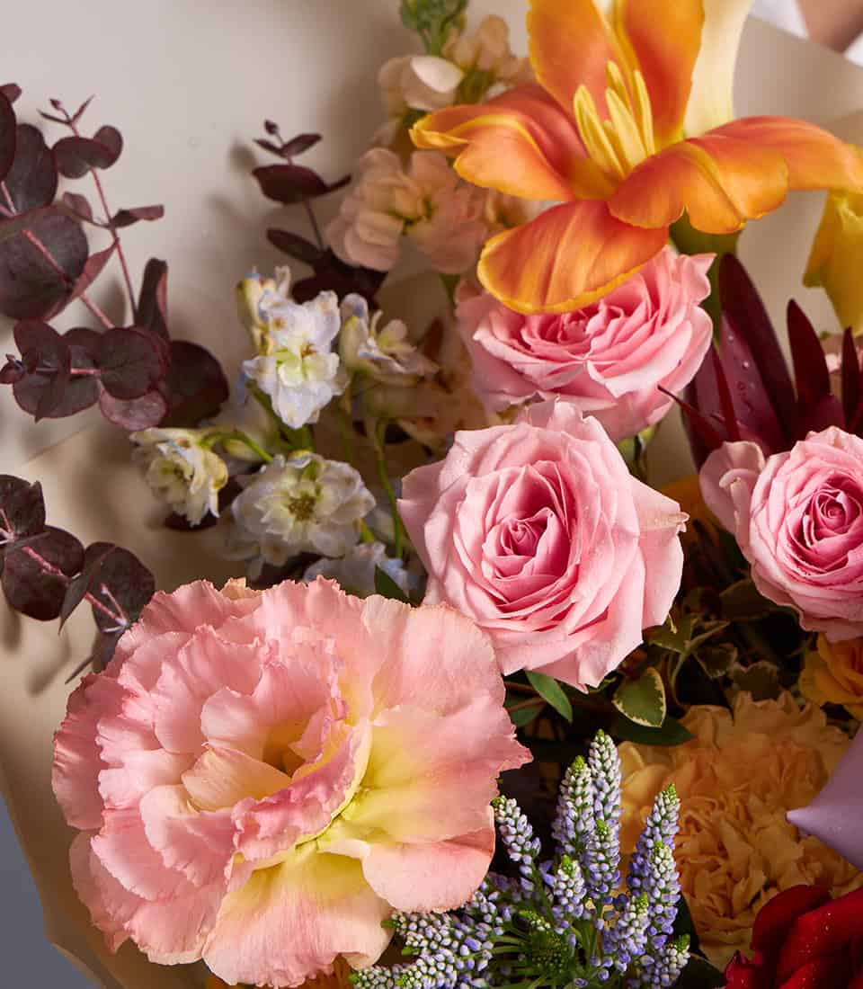 Vibrant bouquet of pink roses, orange lilies, and pastel wildflowers with eucalyptus greenery