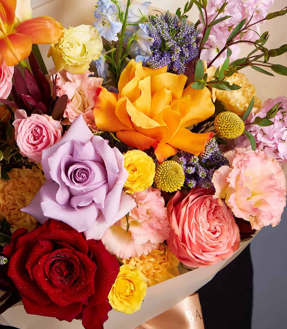 Vibrant mixed bouquet of orange lilies, roses, and pastel wildflowers with fresh water droplets