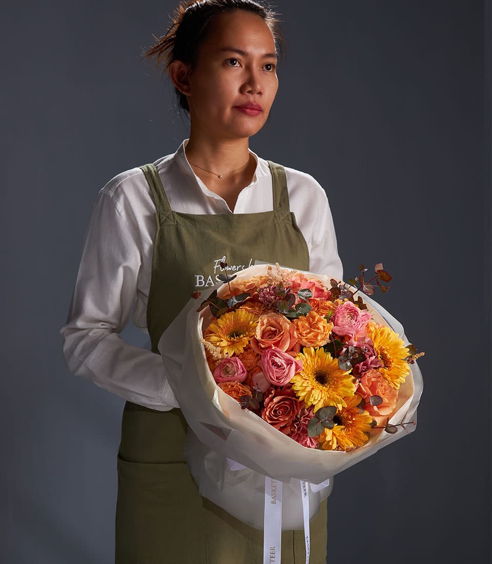 Vibrant mixed bouquet of orange gerberas, pink and orange roses with dried foliage, wrapped in white paper and ribbon