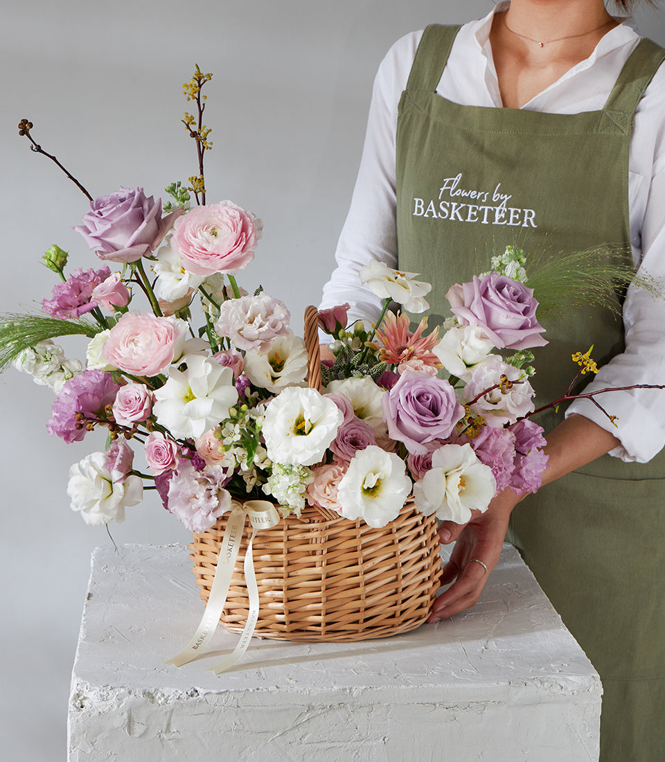 Lavender Grace wicker flower basket with pink roses, purple ranunculus, and white lisianthus