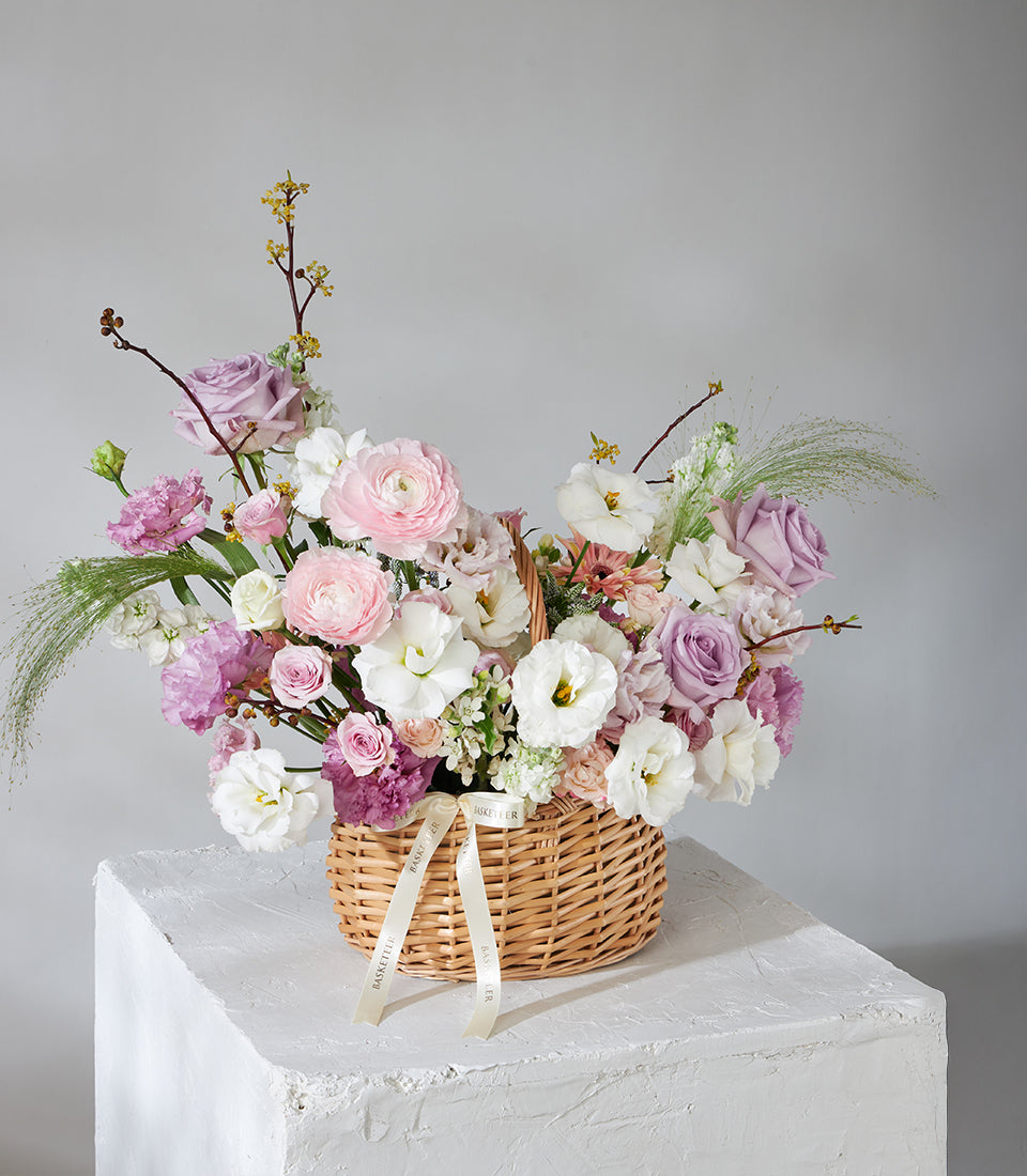 Lavender Grace wicker basket with pink, purple, and white ranunculus, roses, and lisianthus arrangement