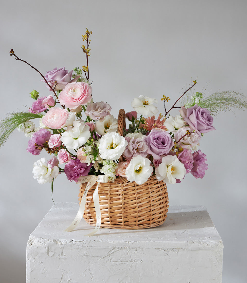 Lavender Grace fresh flower basket with pink ranunculus, purple roses, and white eustoma in wicker with silk ribbon