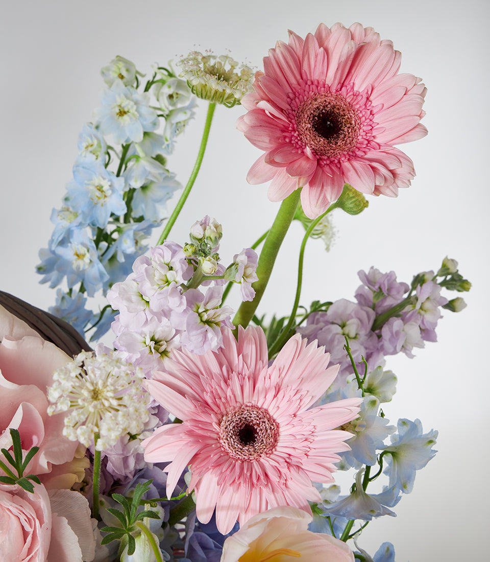Pastel pink gerberas, delphiniums, and stock flowers in a luxury gift basket arrangement