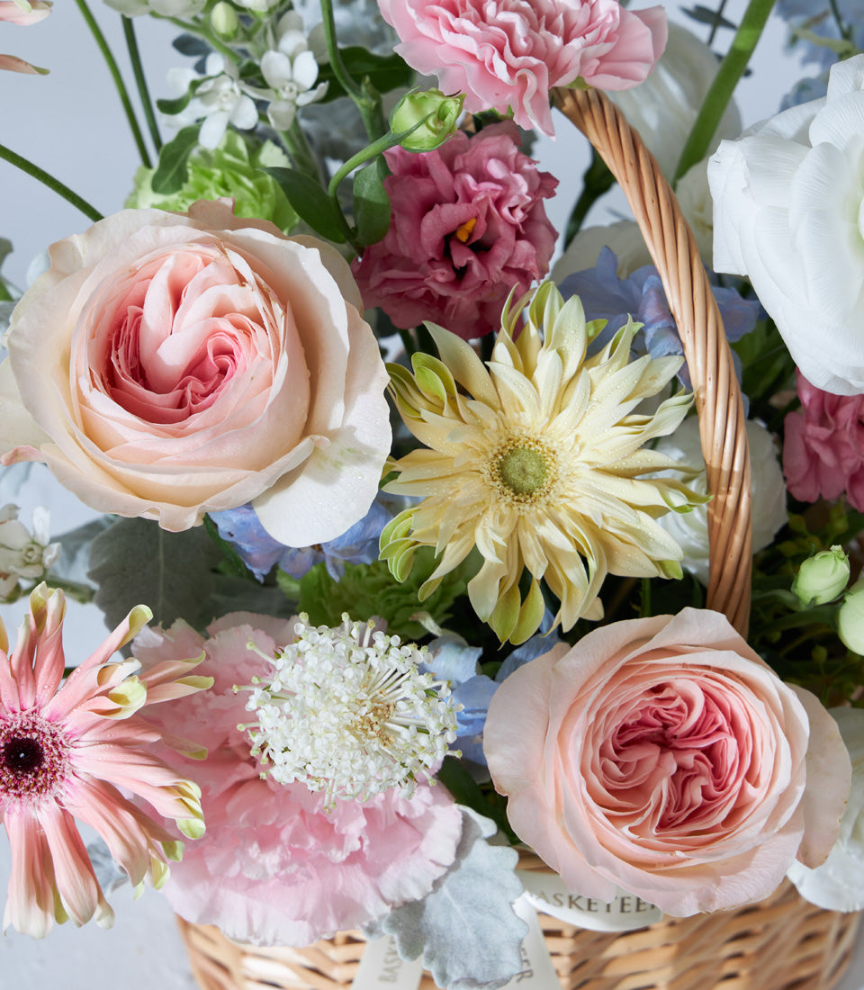 Pastel garden roses, gerbera daisies, and carnations in woven wicker basket for birthday celebrations