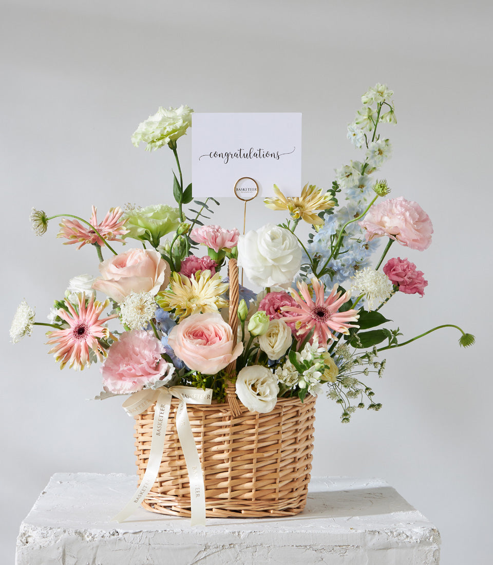 Pastel bloom flower basket with pink, white, and yellow roses in woven wicker for birthday gifts