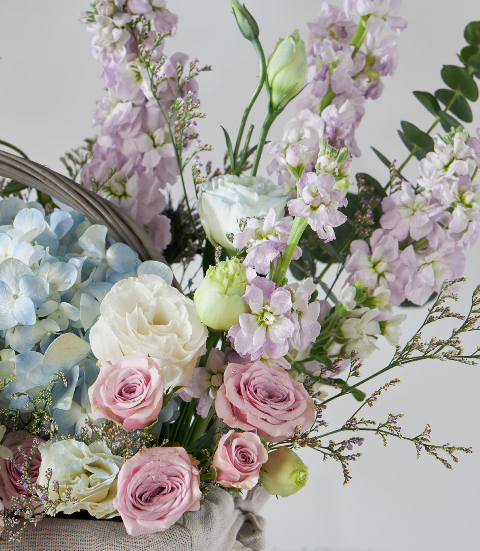 Pastel flower basket with hydrangeas, roses, ranunculus and stock in soft blue, pink and lavender tones