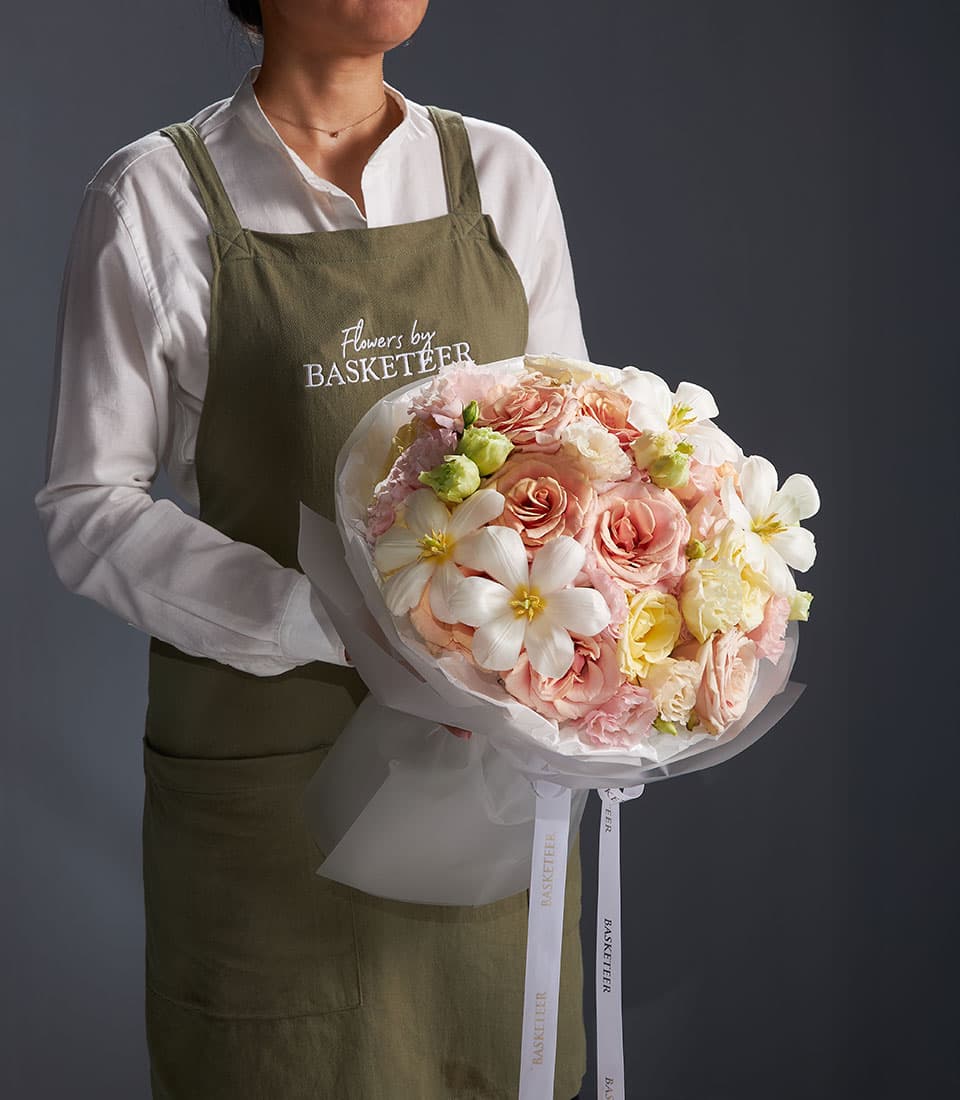 Florist holding Serene Grace mixed bouquet with pink roses, white star flowers, and green accents in white paper wrap