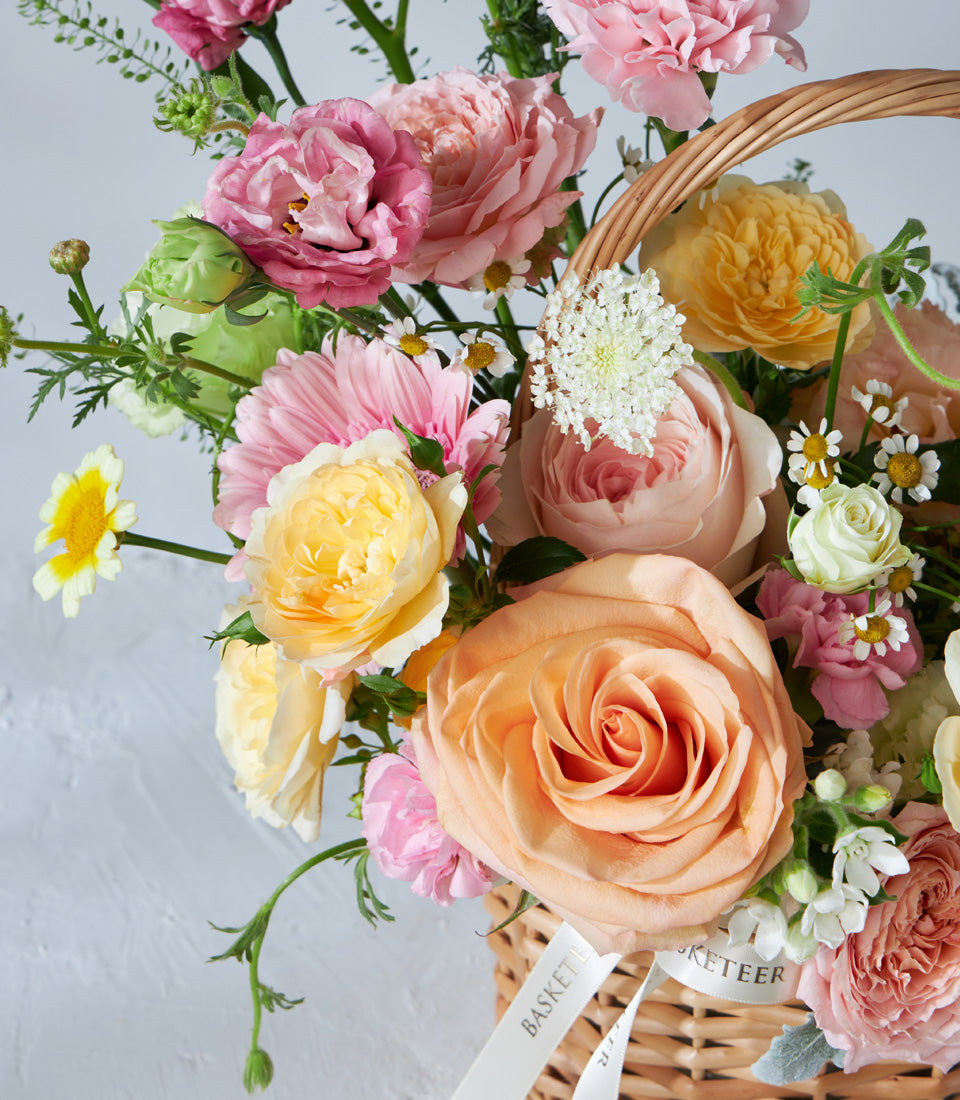 Radiant pink, yellow, and orange roses in woven basket with white ribbon, fresh birthday flowers