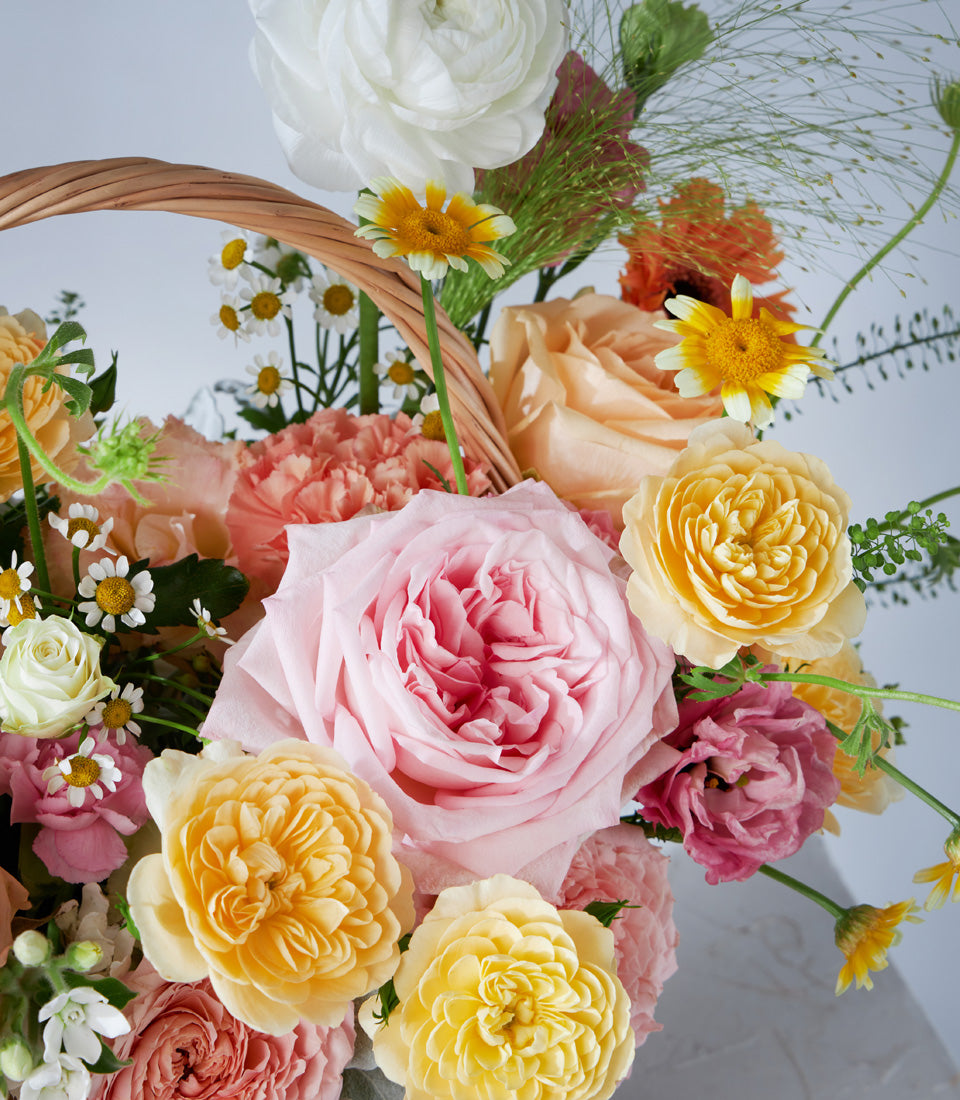 Pink and yellow rose arrangement with ranunculus and gerbera daisies in woven basket, birthday gift