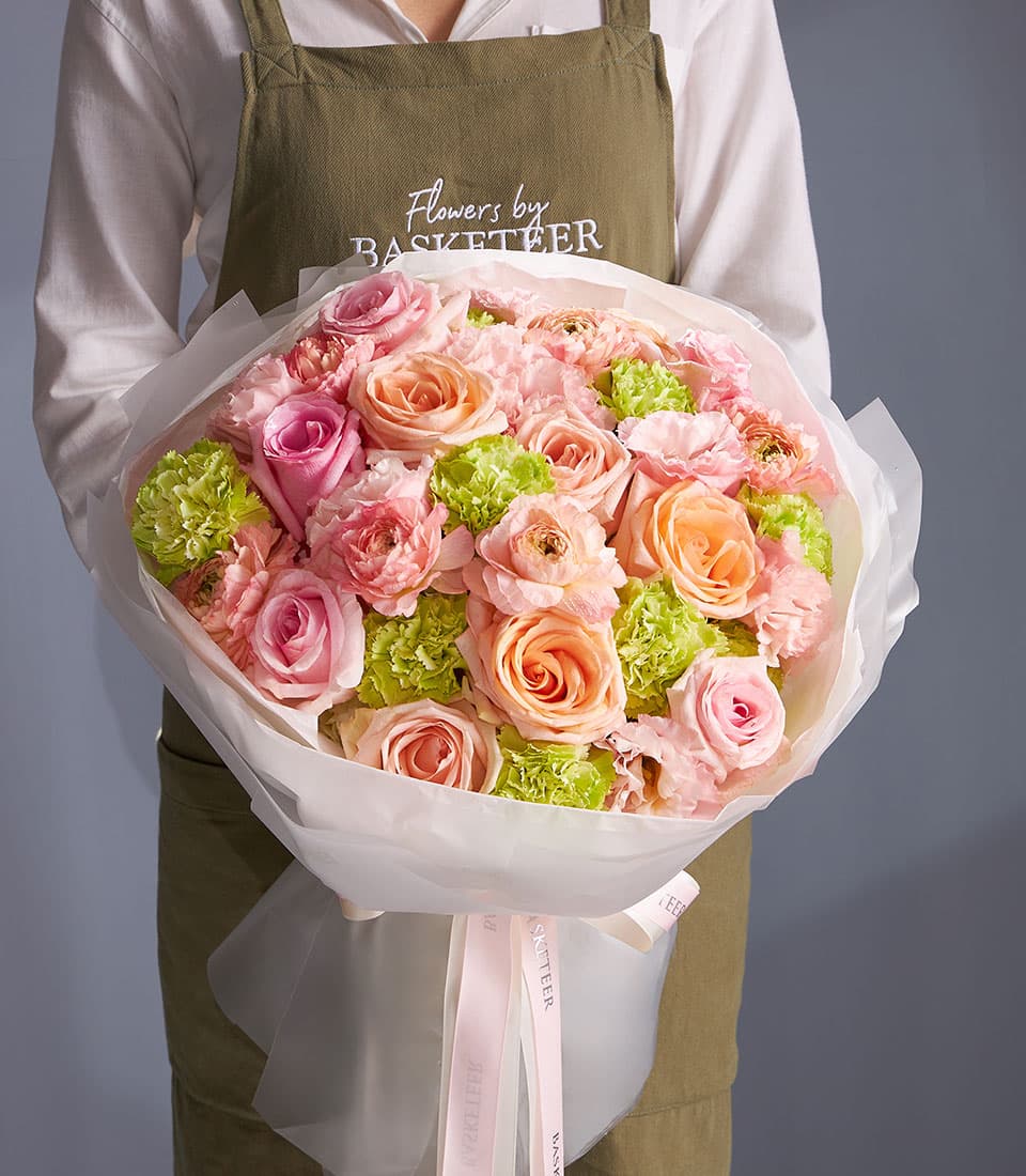 Florist holding pink and peach rose bouquet with green carnations, wrapped in white paper and tied with pink ribbon