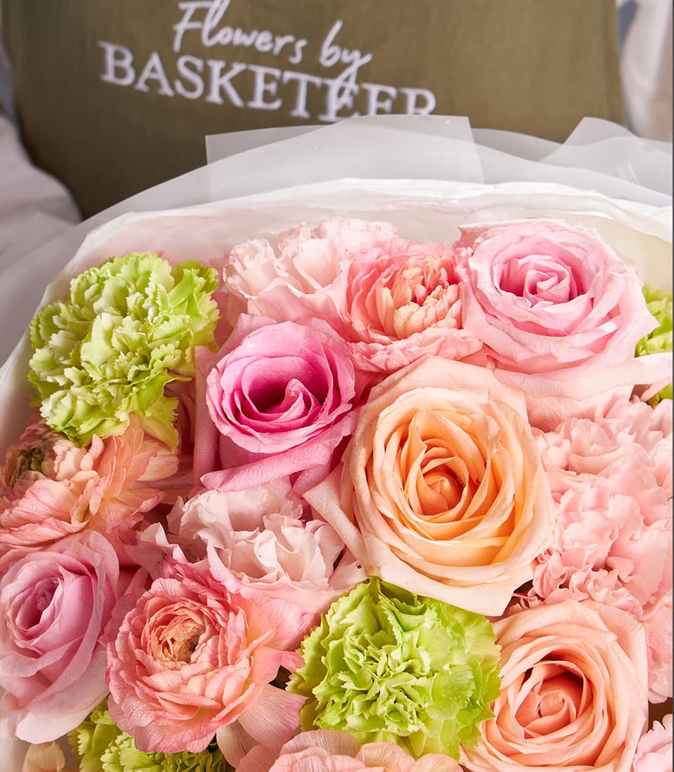 Vibrant mixed bouquet of fresh pink and peach roses and carnations in white paper wrapping