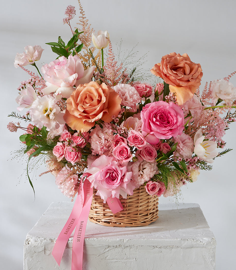Peach and pink roses with tulips in woven wicker basket, premium fresh flower arrangement