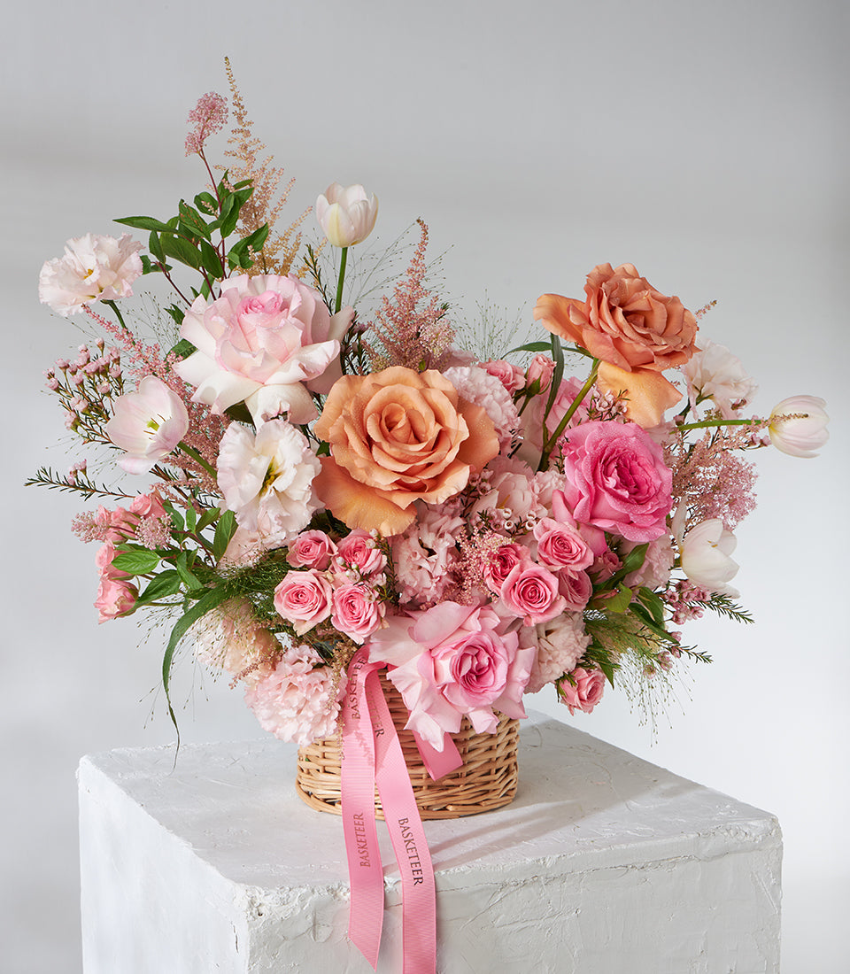 Peach and pink roses with tulips in woven wicker basket, fresh flower gift arrangement