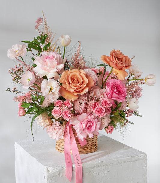 Peach and pink roses with tulips in woven wicker basket, fresh flower gift arrangement