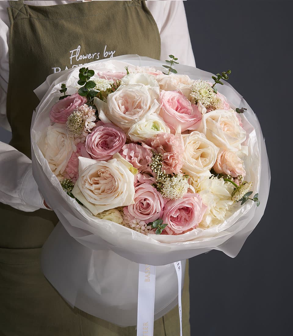Large mixed bouquet of pale pink, cream and white roses with filler flowers wrapped in white paper and ribbon