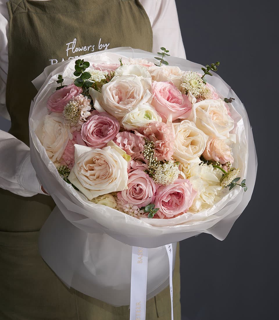 Florist holding oversized mixed rose bouquet in blush, cream, and pink with white filler flowers and green foliage, wrapped
