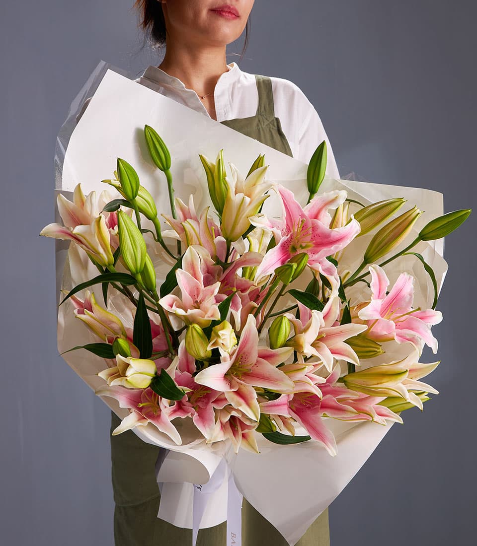 Vibrant pink and white Oriental lily bouquet wrapped in white paper and cellophane with ribbon bow