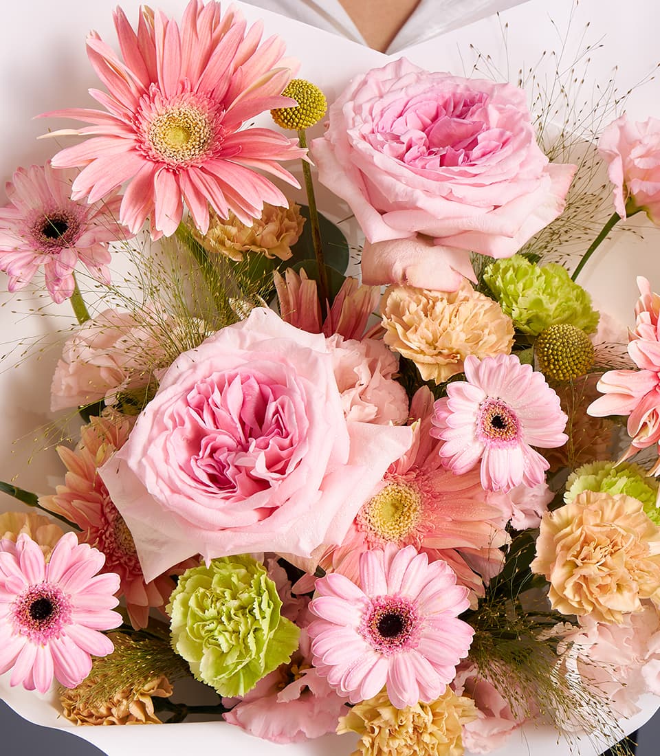 Pastel pink and peach rose and gerbera bouquet with lush garden flowers in soft white wrapping