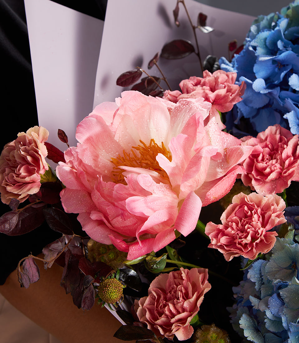 Pink peony luxury bouquet with blue hydrangeas, carnations, and foliage in lavender wrap