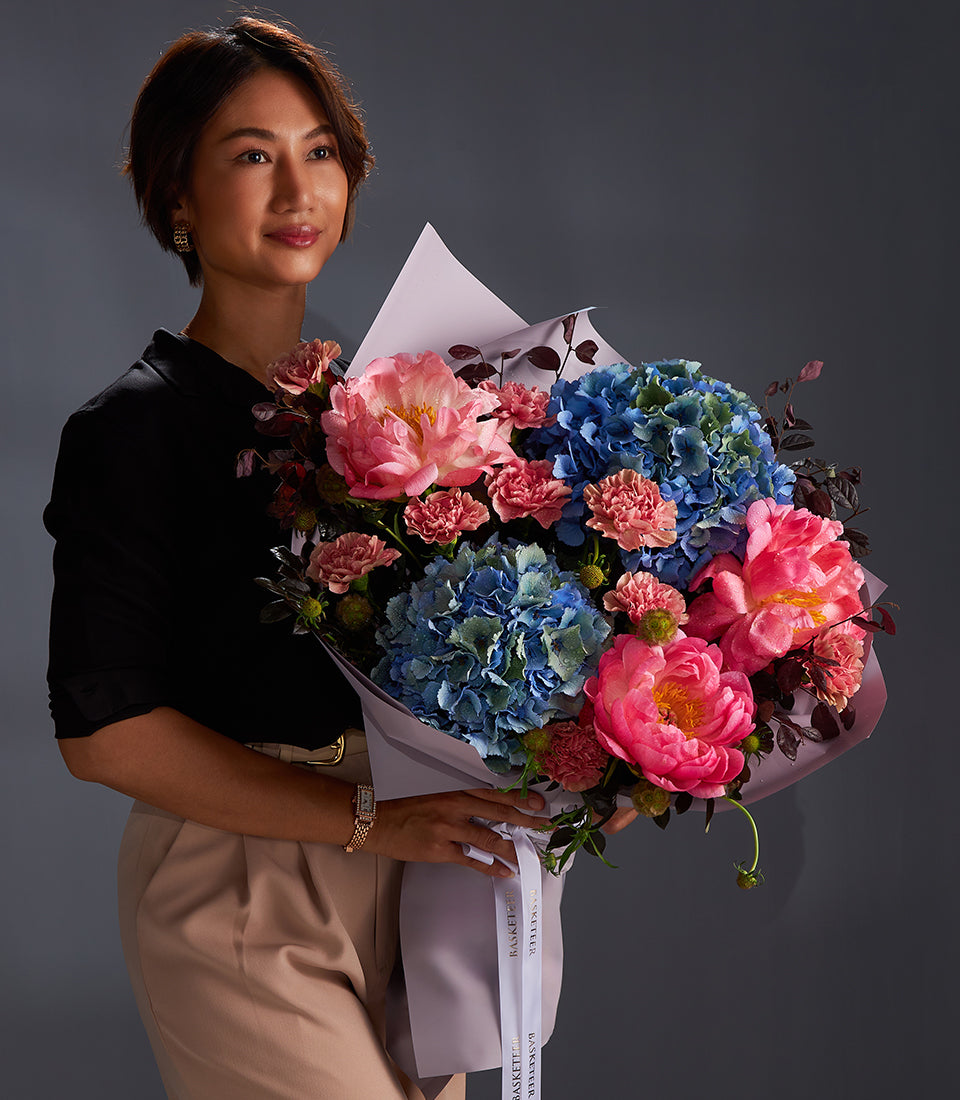 Luxury fresh flower bouquet with pink peonies, blue hydrangeas, and coral carnations wrapped in purple paper