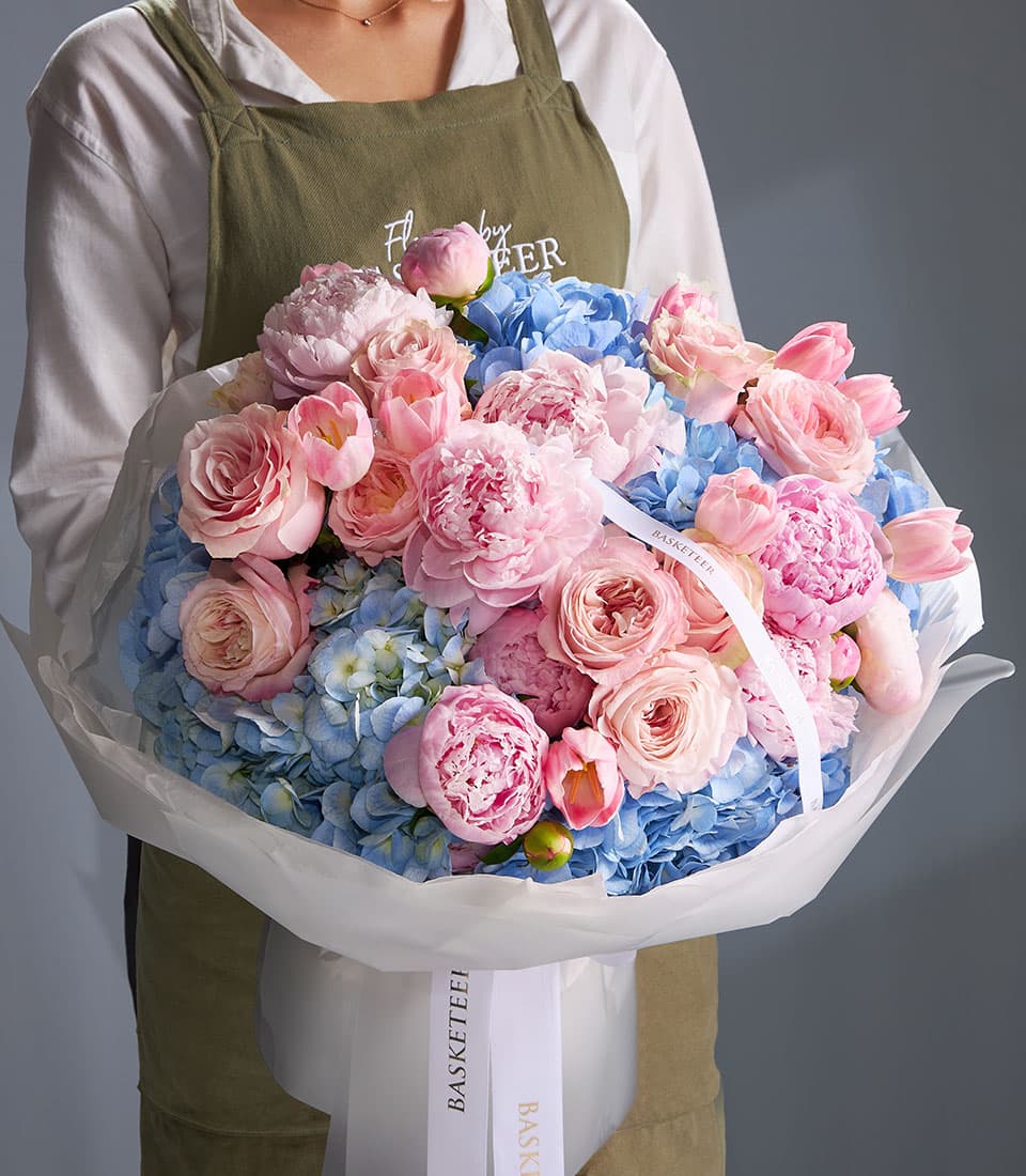 Blush peony and blue hydrangea bouquet with roses and tulips in white wrapped presentation
