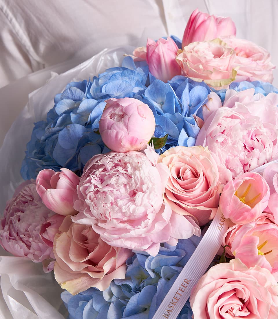 Blush peony and blue hydrangea fresh flower bouquet with roses and tulips, wrapped in white tissue