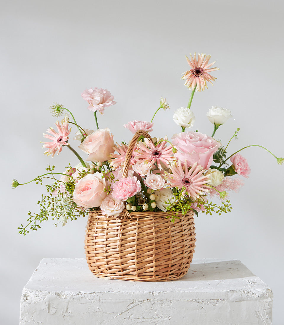 Blush Harmony flower basket with pink roses, gerbera daisies, and white carnations in woven wicker