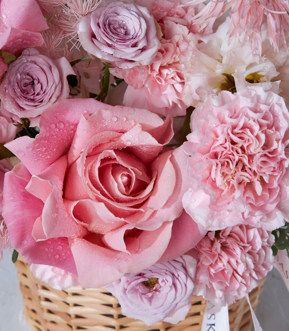 Pink rose and carnation birthday bouquet in woven basket with fresh water droplets
