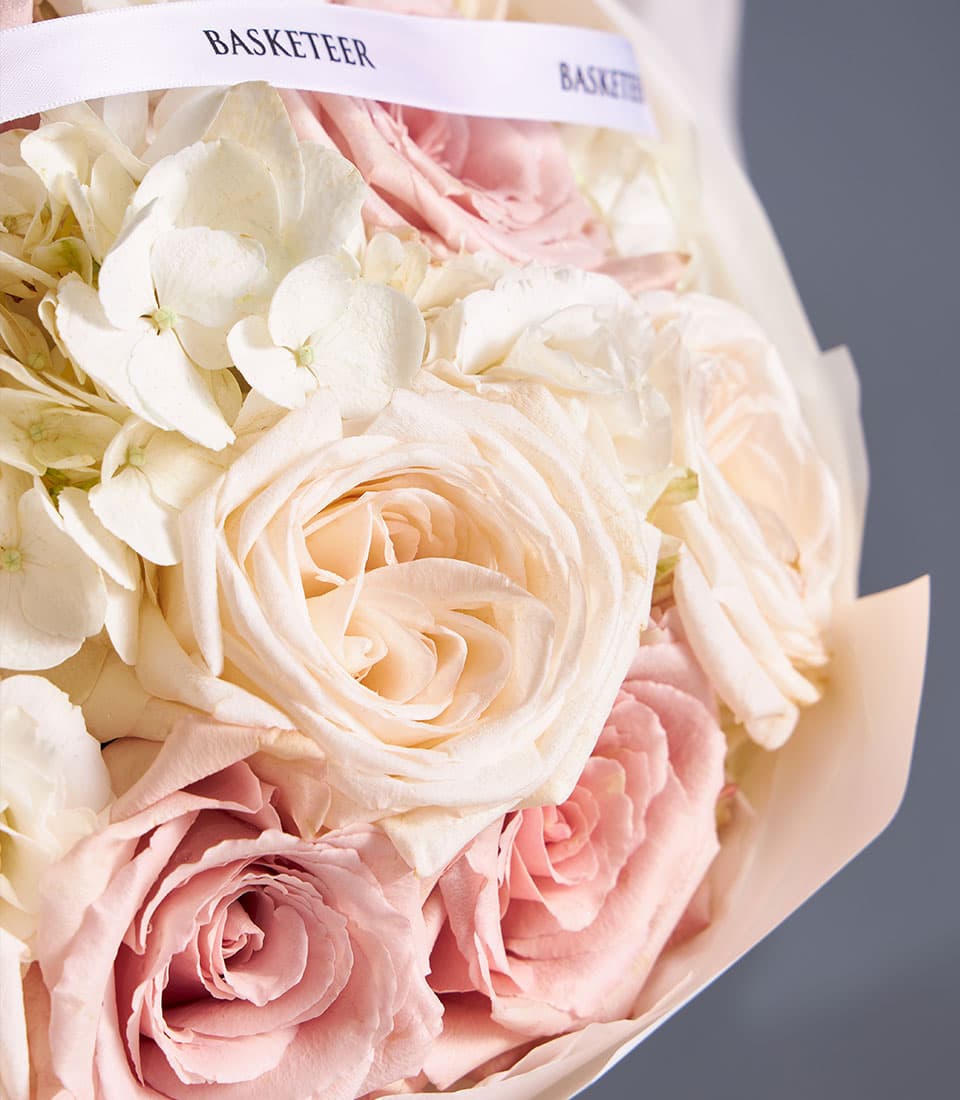 Light pink and cream roses with white hydrangeas fresh flower bouquet wrapped in pale paper