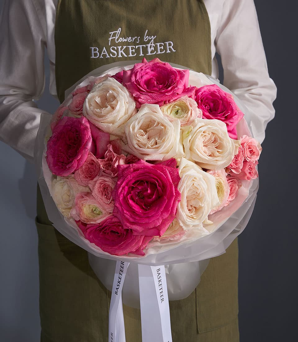 Florist holding large fresh rose bouquet in blush pink and cream with water-kissed petals, wrapped in white tissue and tied