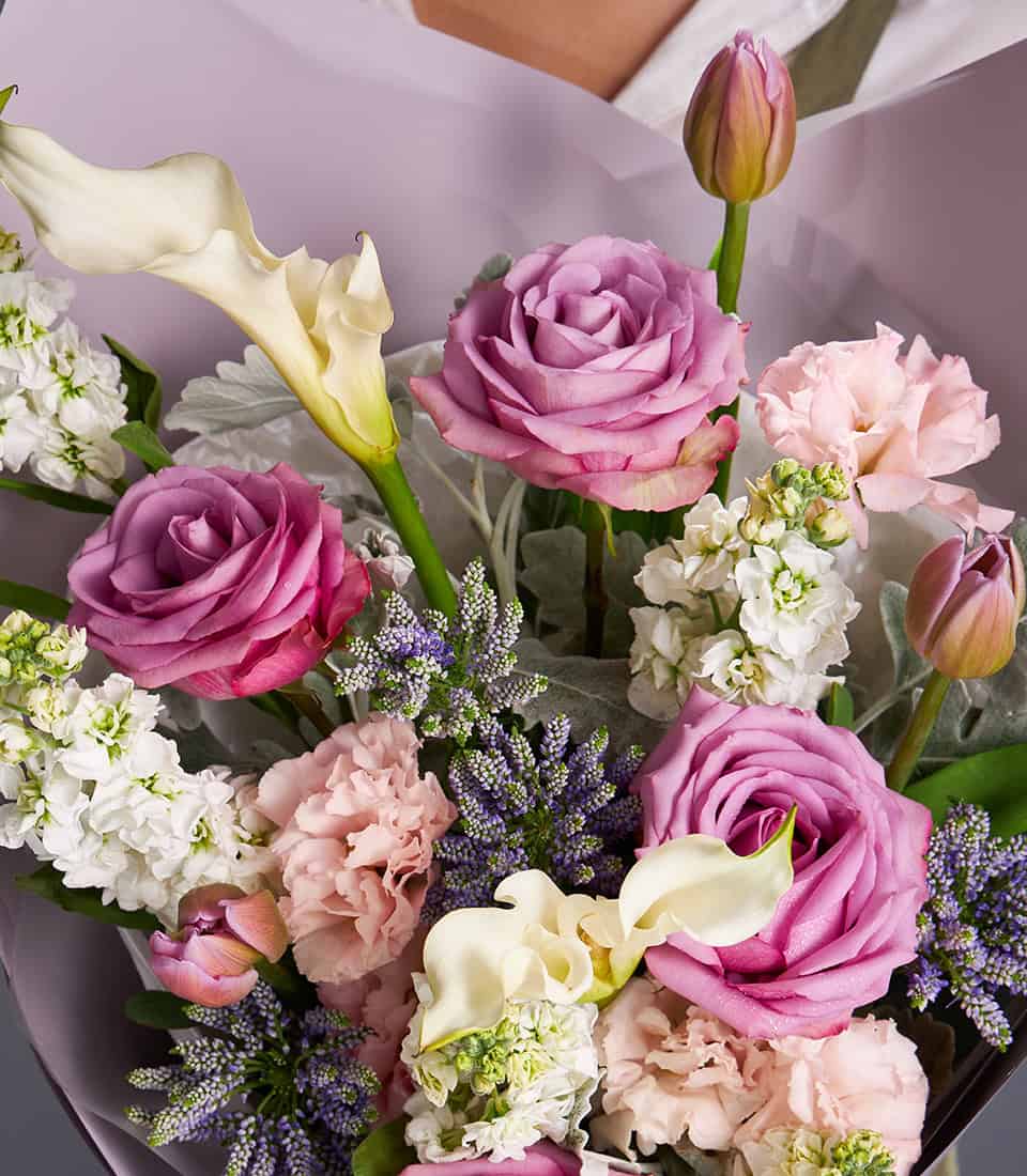 Lavender roses and white calla lilies bouquet with pink carnations and stock flowers, wrapped in purple paper