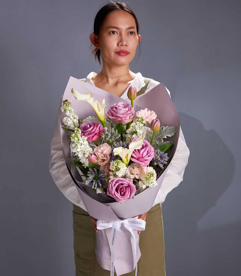 Lavender roses and white calla lilies bouquet wrapped in purple paper with green foliage