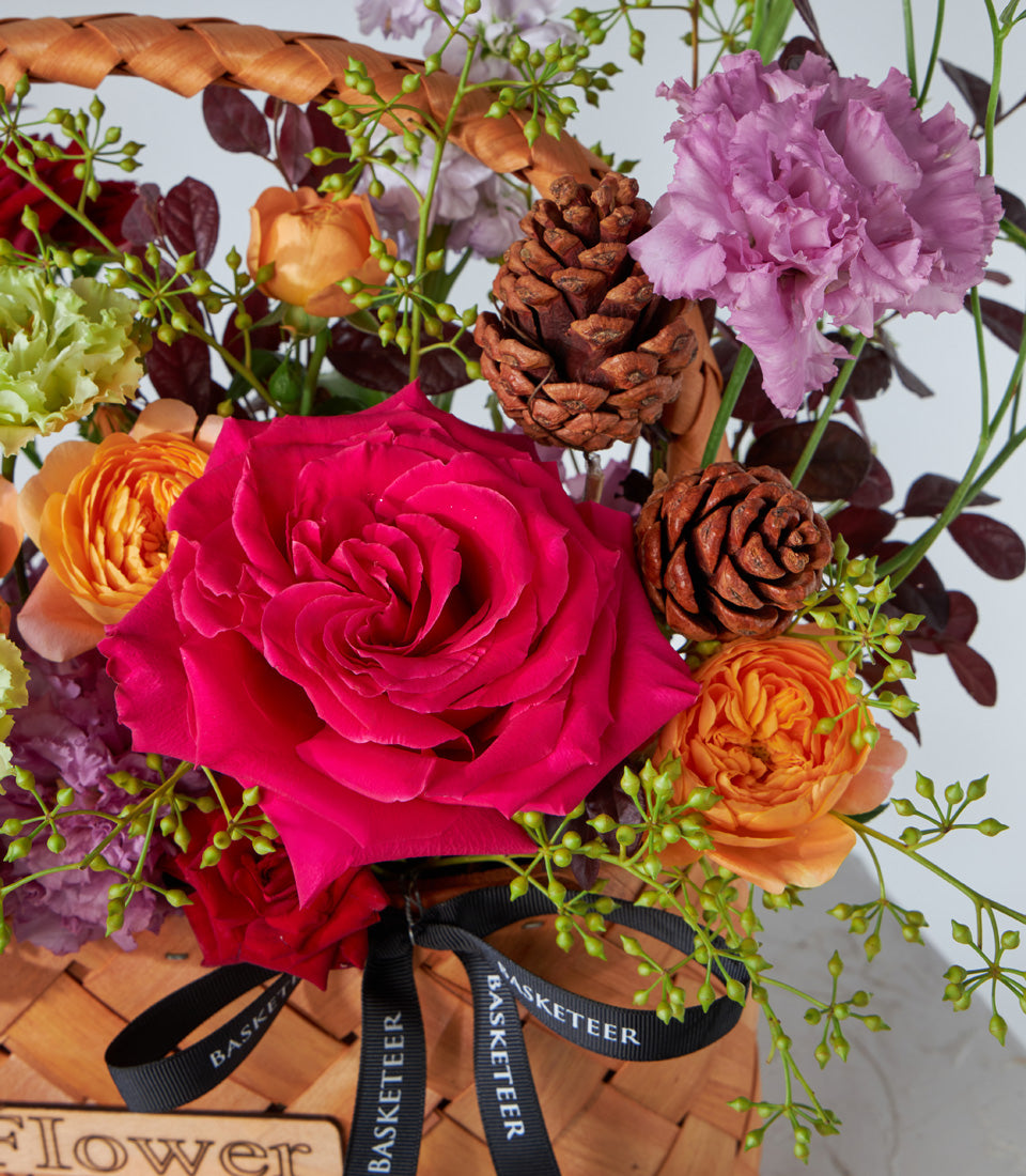 Crimson and orange roses in woven basket with pinecones, birthday flower gift arrangement