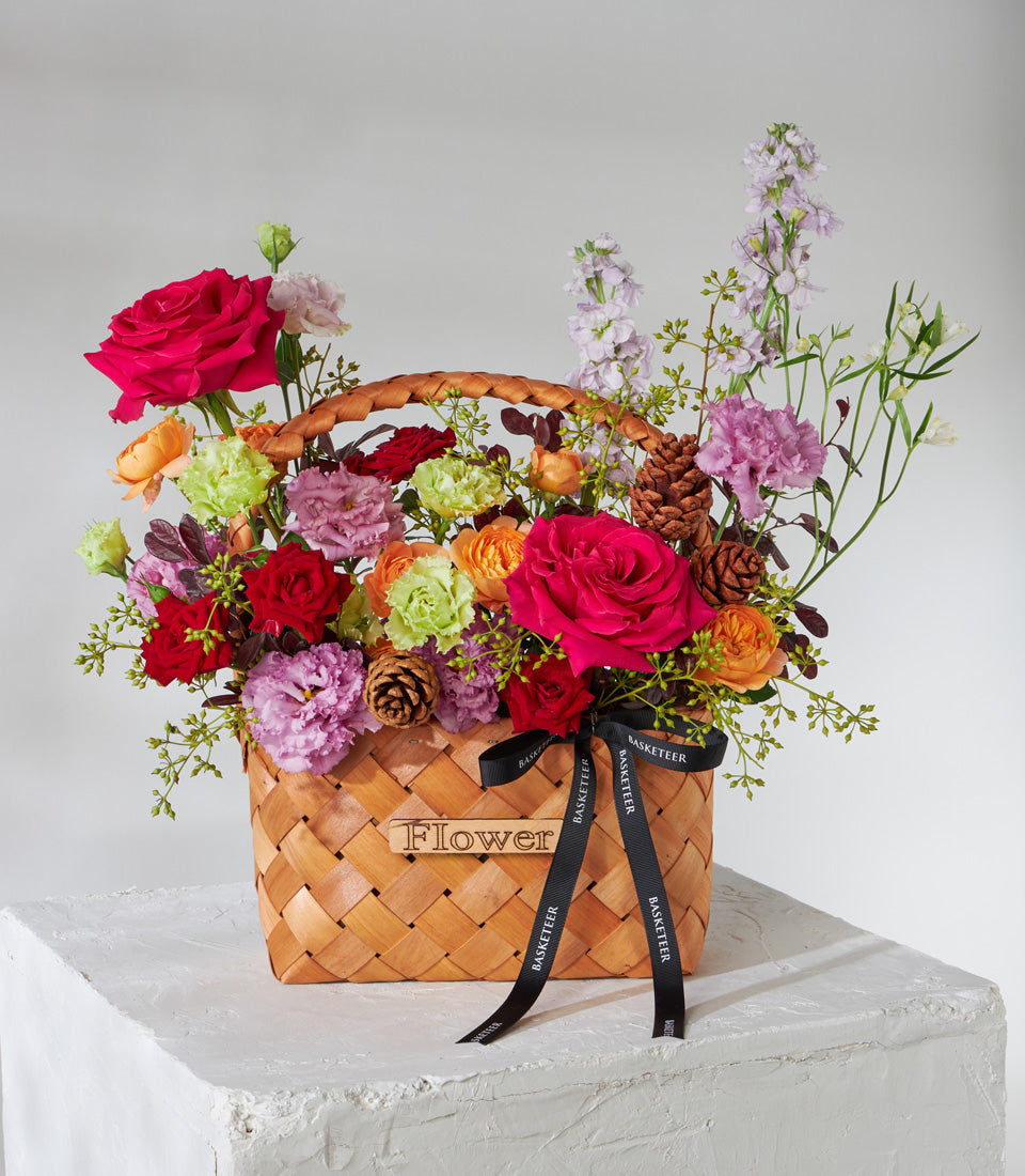 Vibrant crimson and fuchsia roses with mixed carnations and lisianthus in woven basket, perfect for birthdays