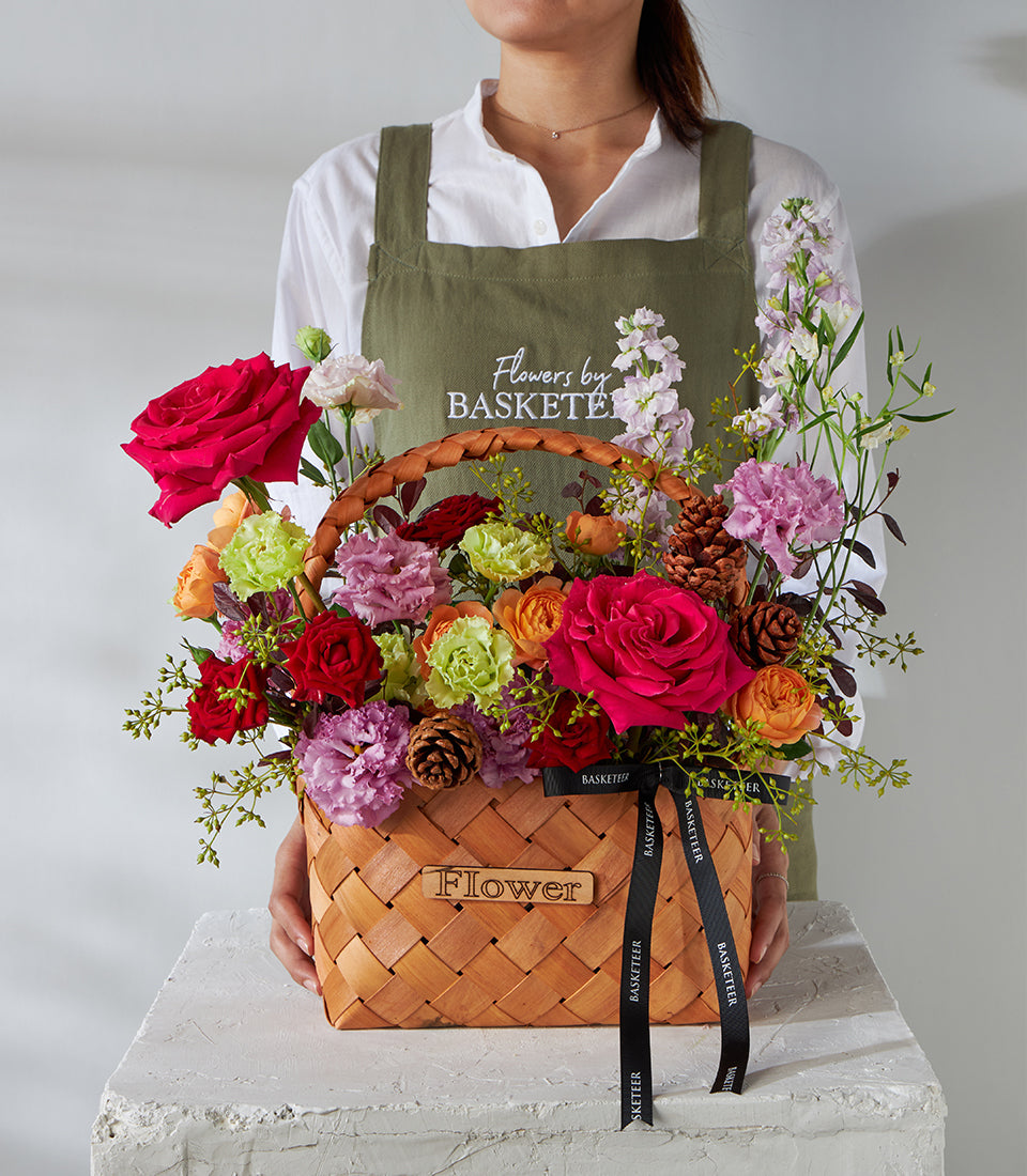 Crimson Elegance woven basket filled with pink and red roses, carnations, and pinecones for birthday celebrations