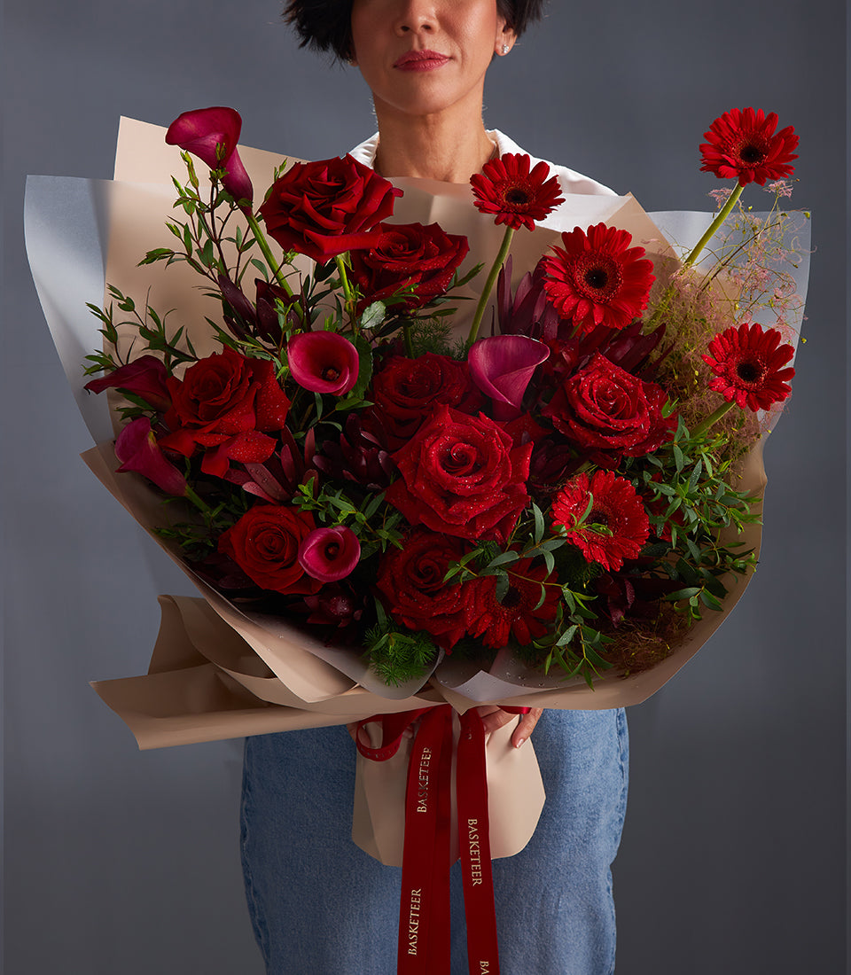 Large crimson bouquet of fresh roses, calla lilies, and gerbera daisies wrapped in kraft paper with red ribbon