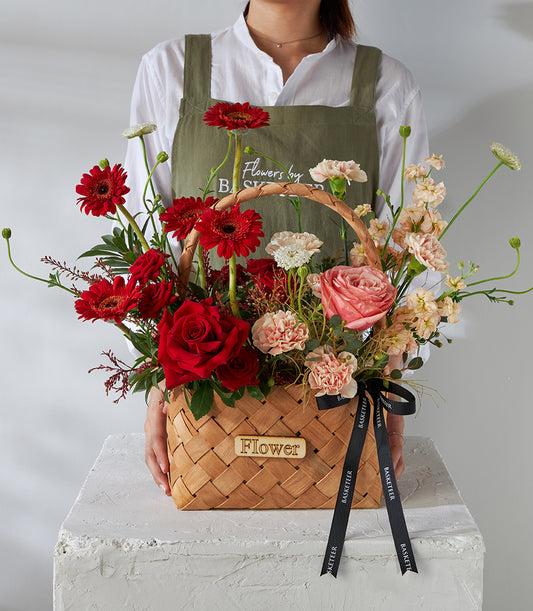 Vibrant red roses and gerbera daisies in woven basket with pink carnations, perfect for birthday celebrations