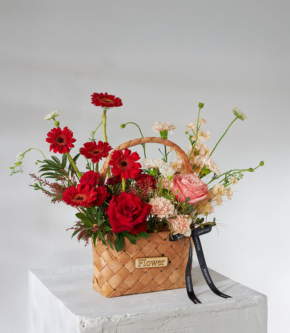 Crimson roses and gerbera celebration basket with pink carnations in woven wooden carrier