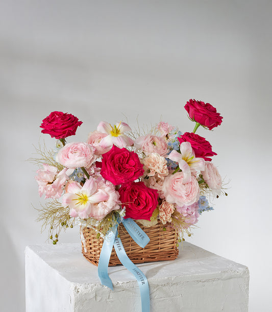 Red roses, pink ranunculus and white lilies in woven basket with blue satin ribbon