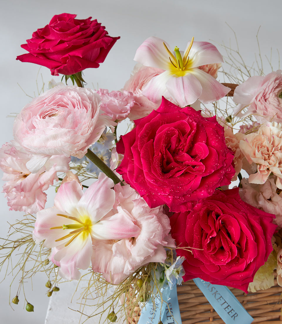 Red roses, pink ranunculus and white lilies in woven basket with light blue ribbon