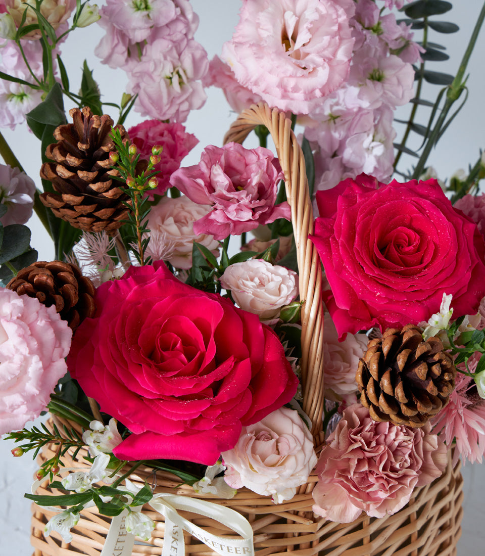 Crimson Charm flower basket with fuchsia and pink roses, pinecones, and cream ribbon for birthday gifts