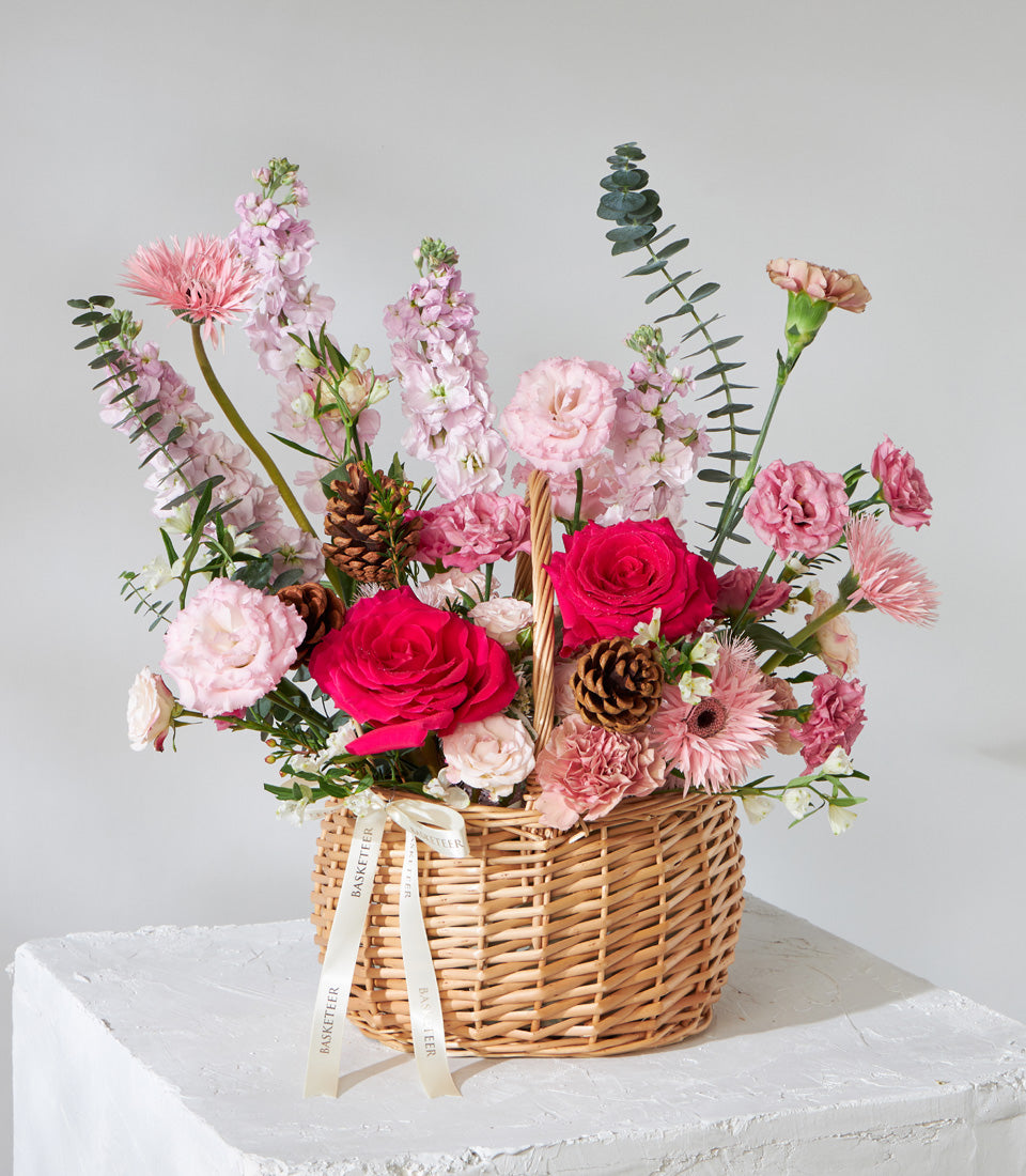 Vibrant pink roses and gerbera daisies in woven wicker basket with eucalyptus, birthday flower gift