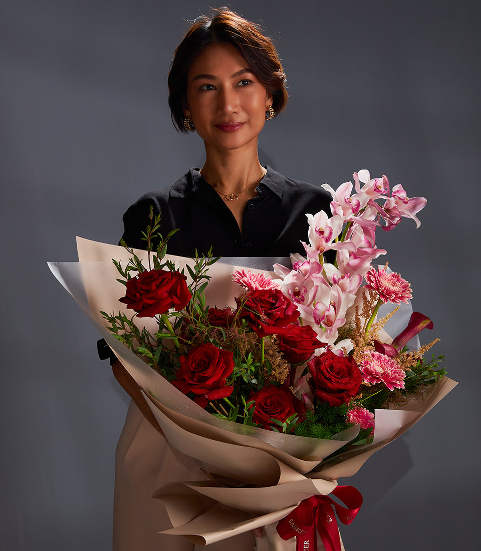 Elegant bouquet of red roses, pink orchids and gerberas wrapped in kraft paper with red satin ribbon