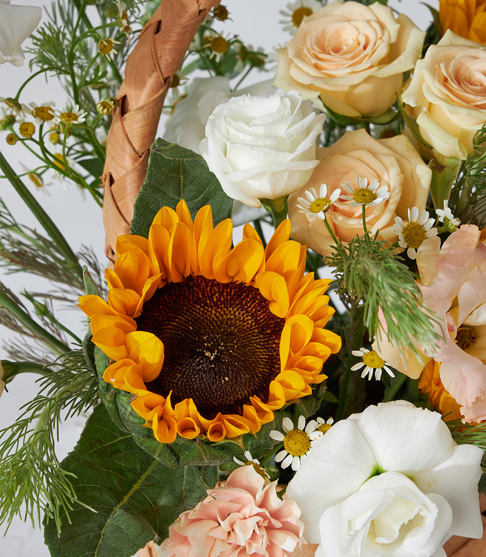 Sunflower, white roses, and peach spray roses in woven basket bouquet for birthday