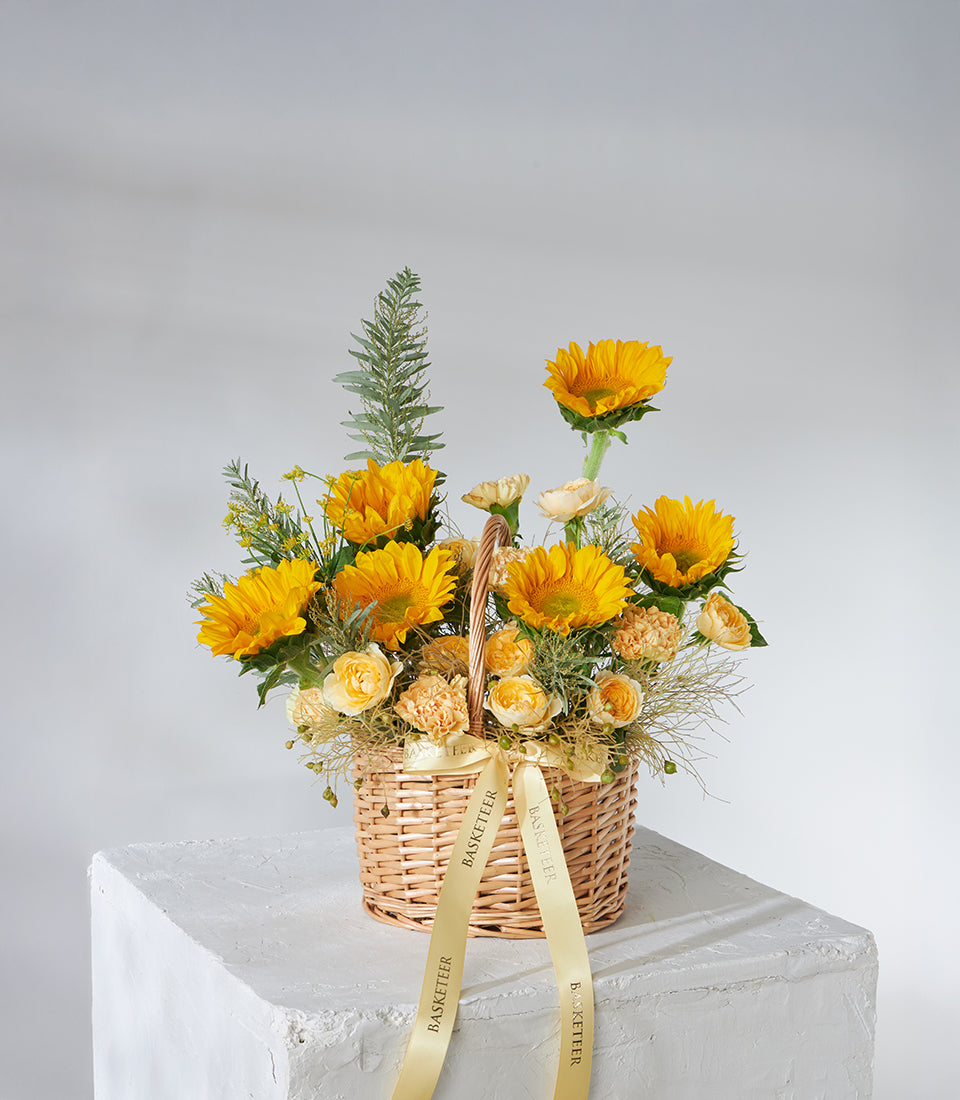 Vibrant sunflowers and yellow roses in wicker basket with golden ribbons