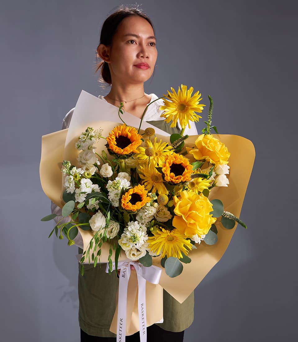 Vibrant yellow sunflower and rose bouquet with white stock flowers and eucalyptus greenery, wrapped in tan paper with white