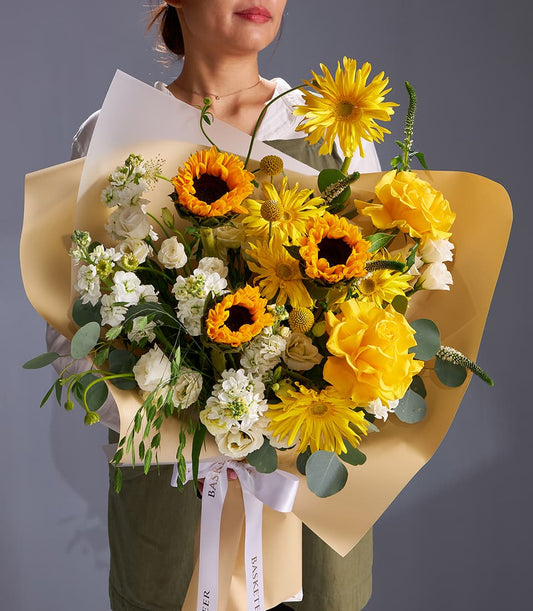 Vibrant yellow sunflower and rose bouquet with eucalyptus, wrapped in kraft paper and white ribbon
