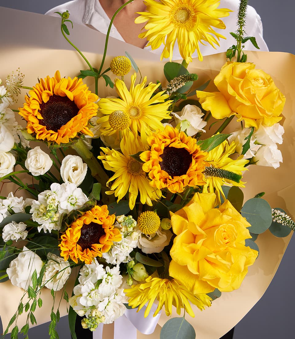 Vibrant yellow sunflower and white rose bouquet with gerbera daisies in kraft paper wrapping