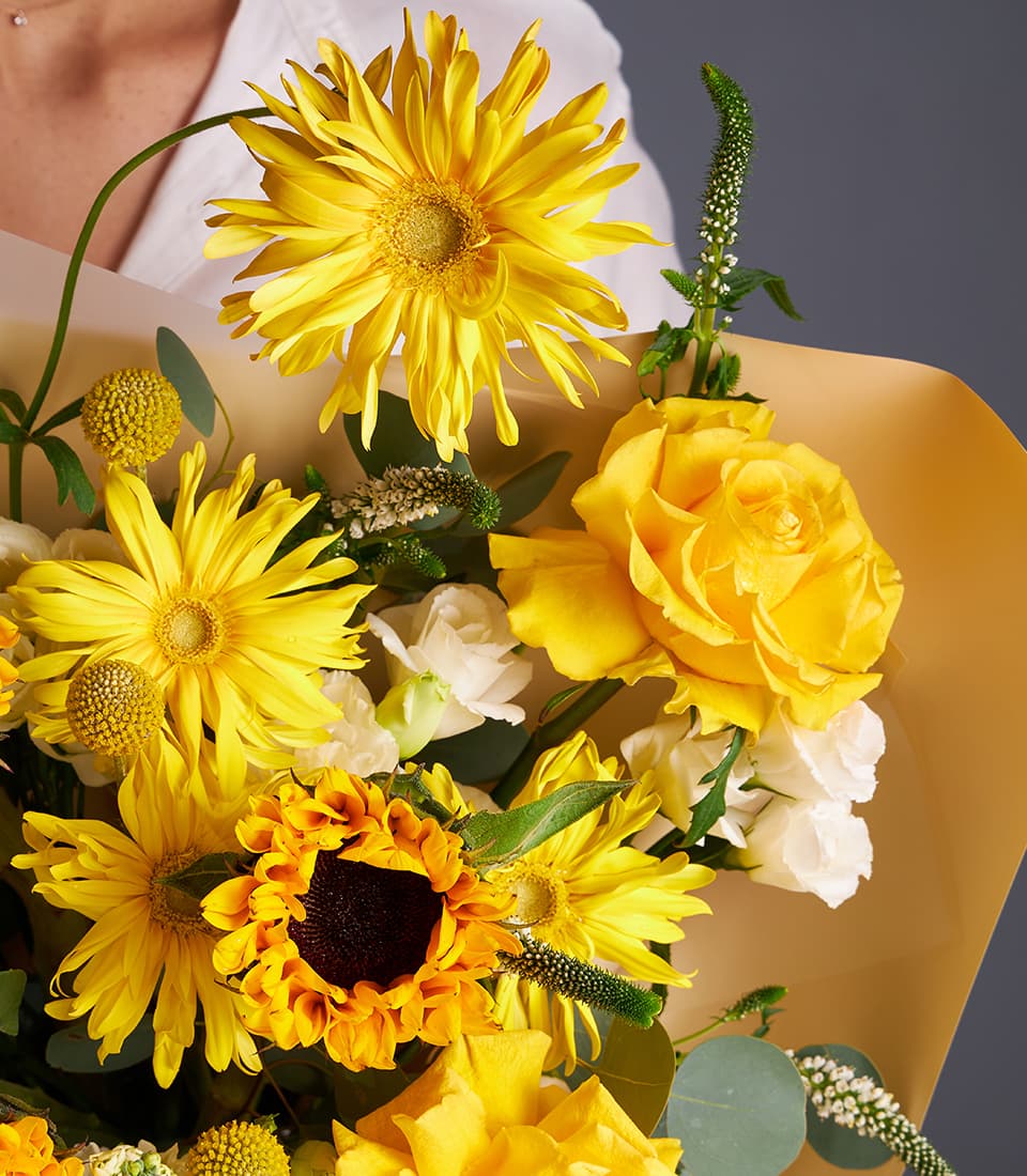 Vibrant yellow roses, sunflowers and white flowers bouquet wrapped in kraft paper