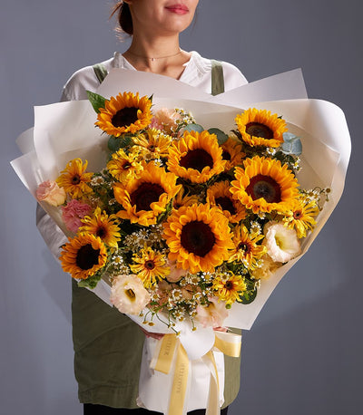 Vibrant sunflower and daisy bouquet wrapped in white paper with yellow ribbon bow
